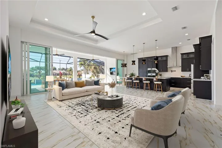 AI Staged photo. Living area featuring a sunroom, a tray ceiling, recessed lighting, ceiling fan, and light marble finish floors