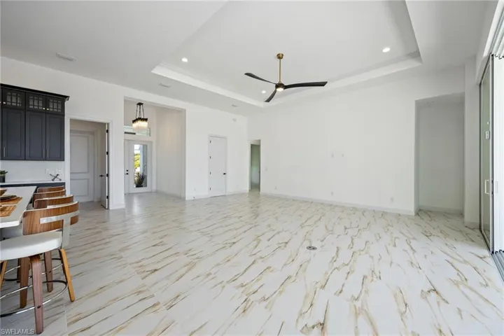 Unfurnished living room featuring light marble finish floors, ceiling fan, recessed lighting, and a raised ceiling