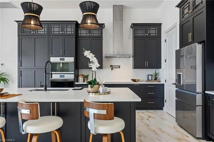 Kitchen with a breakfast bar area, glass insert cabinets, wall chimney exhaust hood, stainless steel appliances, and light marble finish floors