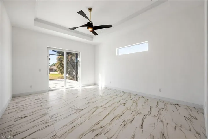 Empty room with a tray ceiling, light marble finish floors, and ceiling fan