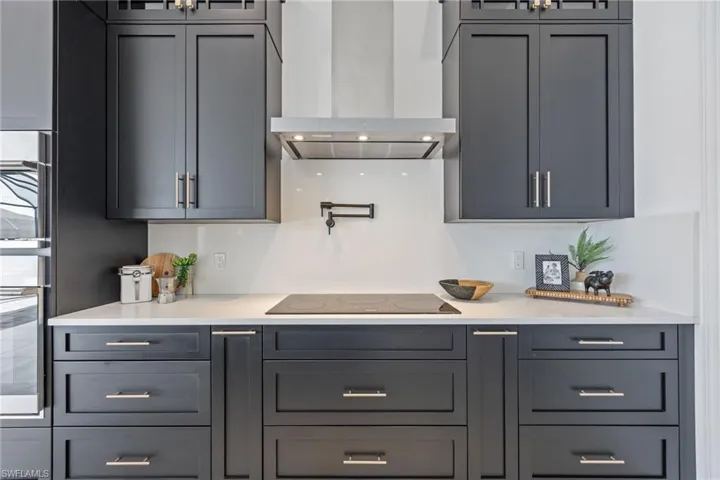 Kitchen with glass insert cabinets, wall chimney exhaust hood, light stone countertops, and black electric stovetop