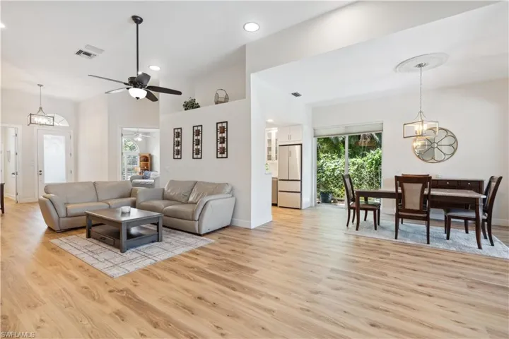 Living room with a towering ceiling, light wood-type flooring, and ceiling fan with notable chandelier
