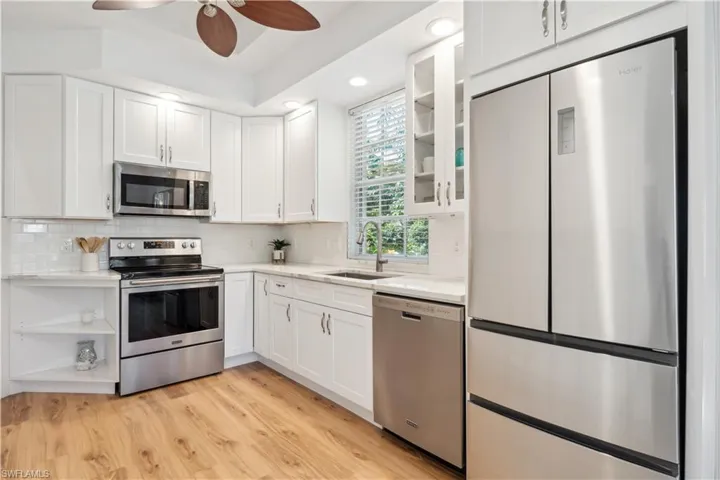 Kitchen with appliances with stainless steel finishes, white cabinetry, ceiling fan, and light hardwood / wood-style floors