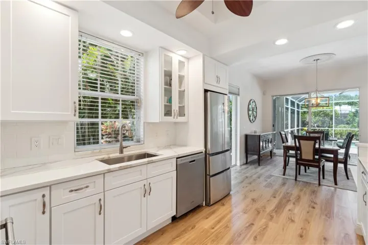 Kitchen with light hardwood / wood-style flooring, tasteful backsplash, stainless steel appliances, ceiling fan with notable chandelier, and sink