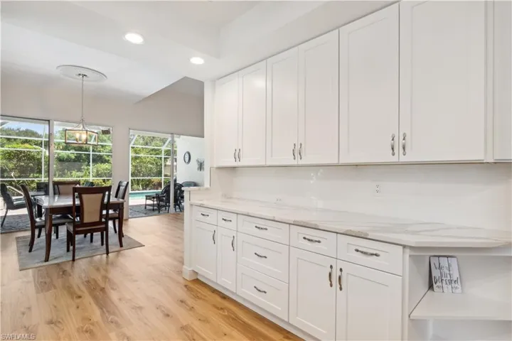 Kitchen with light stone countertops, light hardwood / wood-style flooring, pendant lighting, white cabinetry, and a chandelier