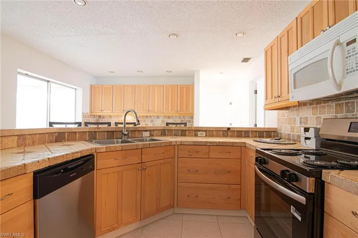 Kitchen featuring stainless steel appliances, backsplash, tile counters, light tile patterned flooring, and a textured ceiling