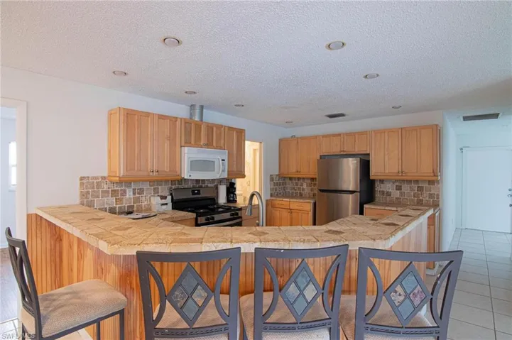 Kitchen with a kitchen breakfast bar, stainless steel appliances, tasteful backsplash, a peninsula, and tile countertops