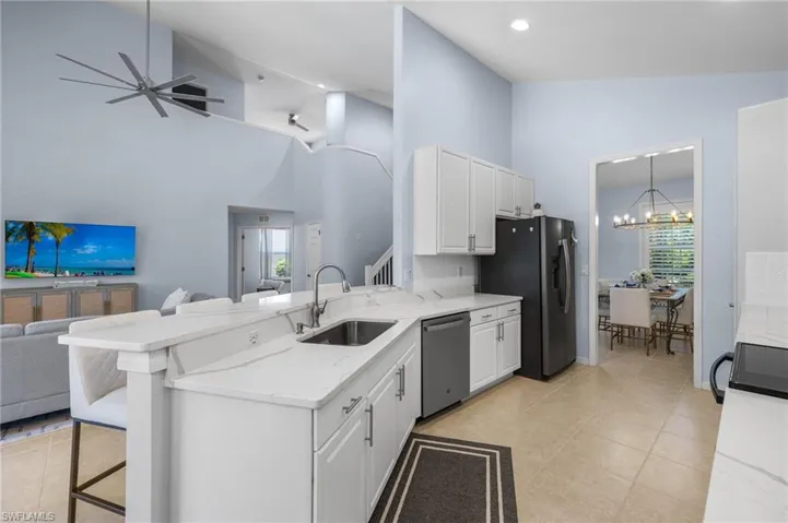 Kitchen with ceiling fan with notable chandelier, high vaulted ceiling, sink, dishwasher, and a kitchen bar