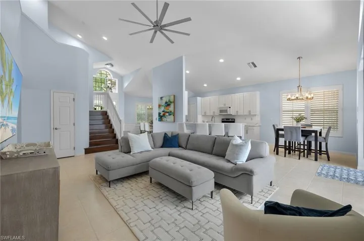 Tiled living room featuring high vaulted ceiling and ceiling fan with notable chandelier
