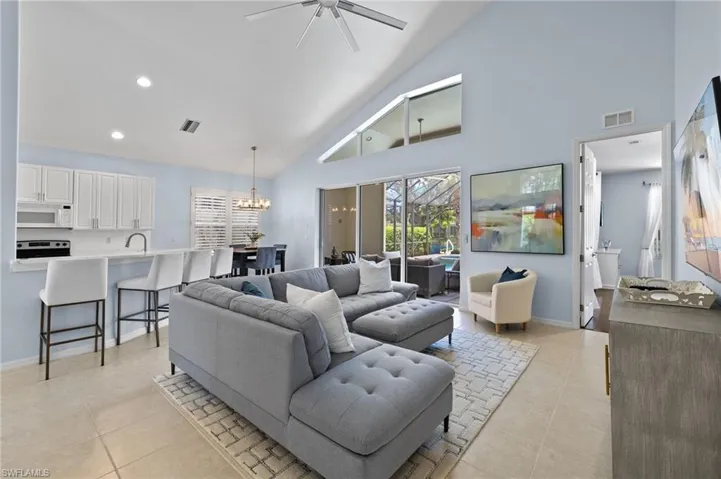 Living room featuring high vaulted ceiling, sink, light tile floors, and ceiling fan with notable chandelier