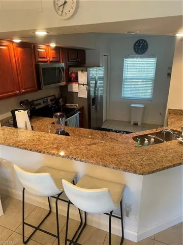 Kitchen featuring a breakfast bar, light stone countertops, stove, light tile patterned floors, and sink