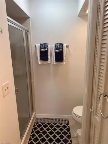 Bathroom featuring a shower with door, toilet, and tile patterned flooring