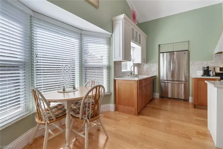 Kitchen with backsplash, sink, light wood-type flooring, white cabinetry, and stainless steel refrigerator