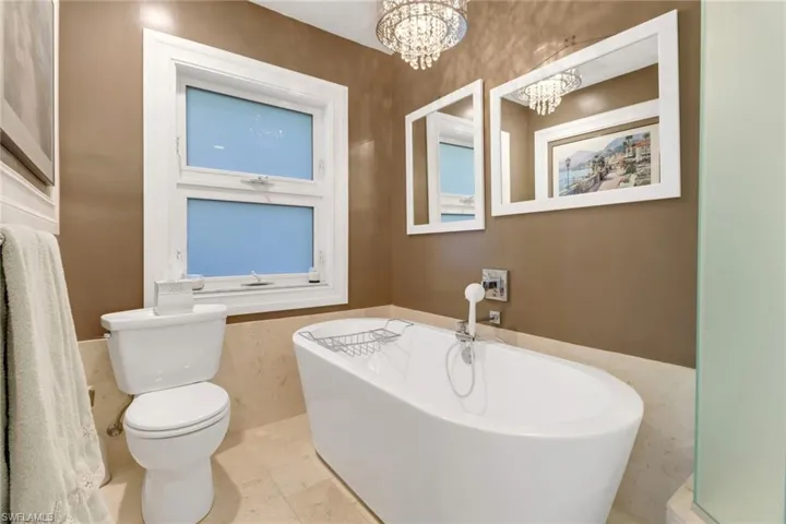 Bathroom featuring a chandelier, tile patterned flooring, a tub to relax in, and toilet
