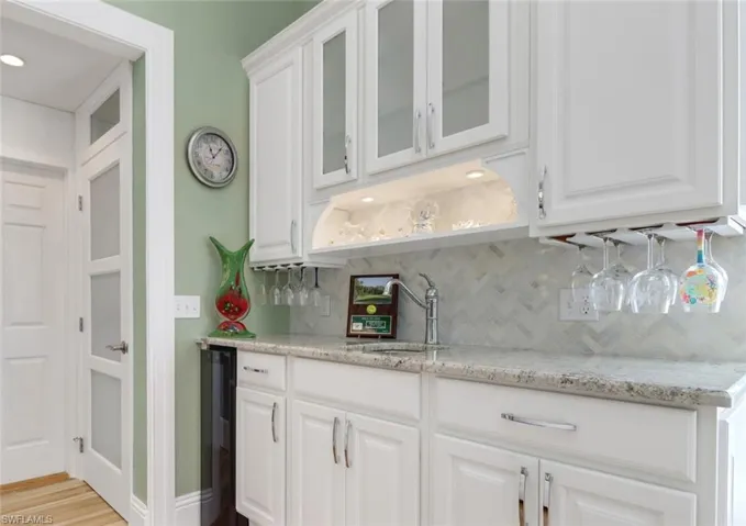 Bar with white cabinets, decorative backsplash, light wood-type flooring, and sink