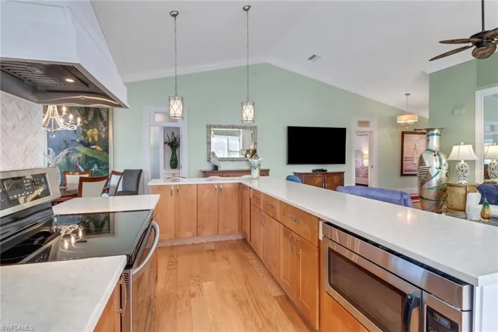 Kitchen featuring light wood-type flooring, custom range hood, stainless steel appliances, vaulted ceiling, and crown molding