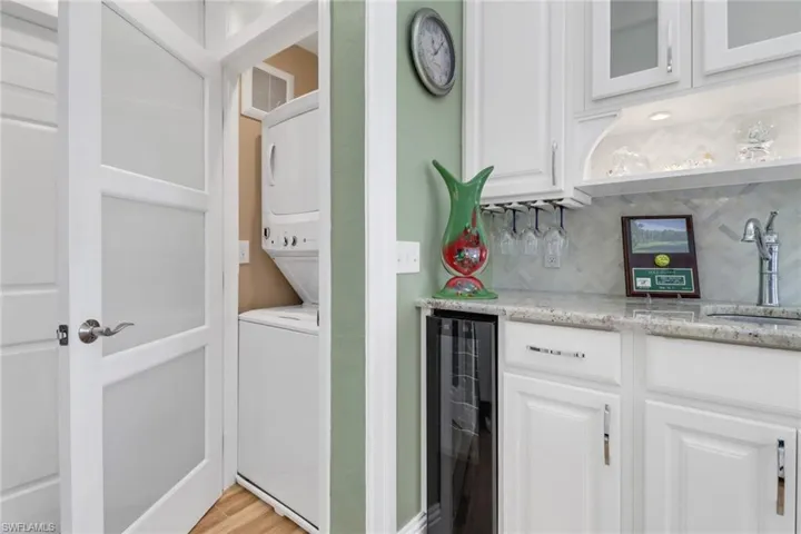 Clothes washing area featuring stacked washer / dryer, light hardwood / wood-style flooring, beverage cooler, and indoor wet bar