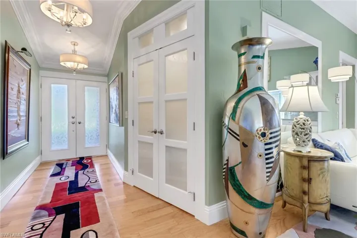 Foyer entrance featuring french doors, light wood-type flooring, an inviting chandelier, and ornamental molding
