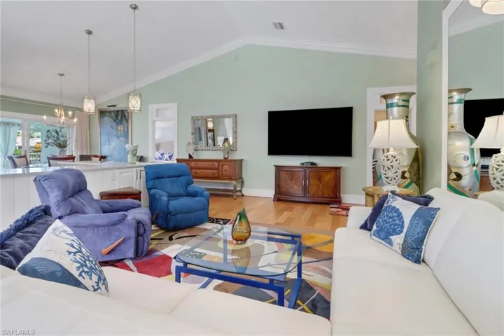 Living room with lofted ceiling, hardwood / wood-style floors, a notable chandelier, and ornamental molding