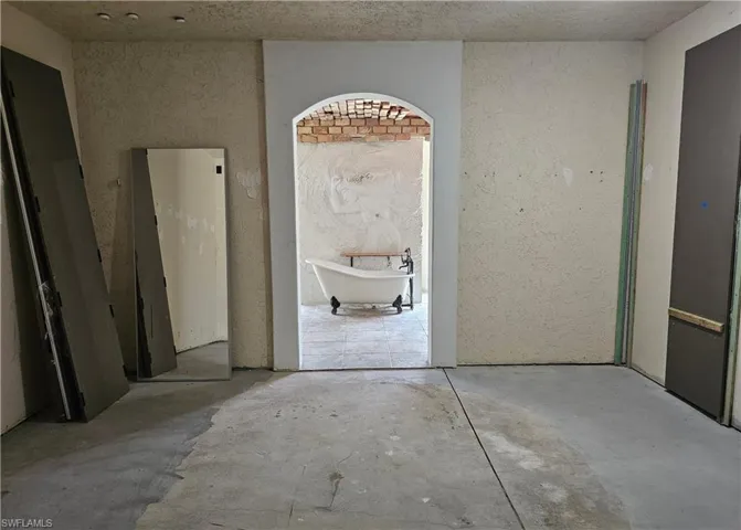Bathroom featuring a textured wall, a freestanding tub, and concrete floors