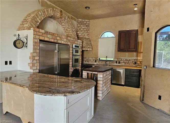 Kitchen featuring stainless steel appliances, dark stone countertops, a peninsula, a center island, and concrete floors