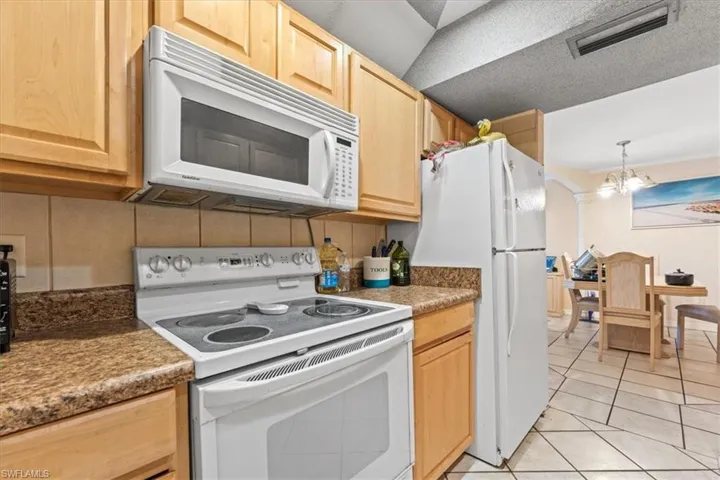 Kitchen featuring white appliances, light brown cabinets, light tile patterned floors, hanging light fixtures, and a chandelier