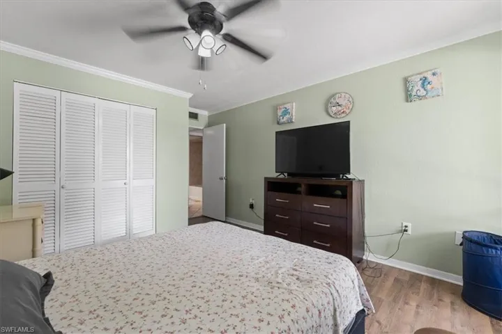 Bedroom featuring crown molding, a closet, baseboards, wood finished floors, and a ceiling fan