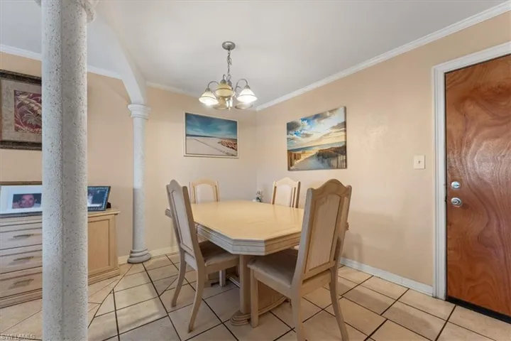 Dining room with ornamental molding, a chandelier, light tile patterned floors, baseboards, and decorative columns