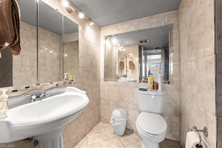 Bathroom featuring tile walls, toilet, a textured ceiling, and tile patterned flooring