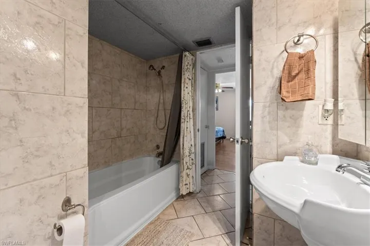 Full bath with shower / bath combination with curtain, tile walls, a sink, a textured ceiling, and tile patterned floors