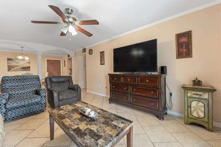 Living room featuring ornate columns, arched walkways, a ceiling fan, light tile patterned floors, and crown molding