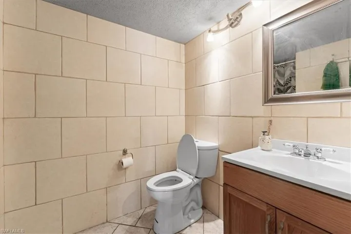 Bathroom with tile walls, toilet, vanity, a textured ceiling, and tile patterned floors