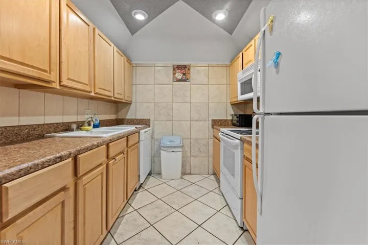 Kitchen with white appliances, a sink, light tile patterned flooring, tile walls, and light brown cabinetry