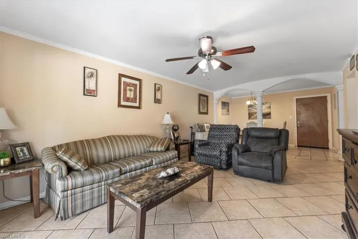 Living room featuring arched walkways, decorative columns, a ceiling fan, ornamental molding, and light tile patterned floors