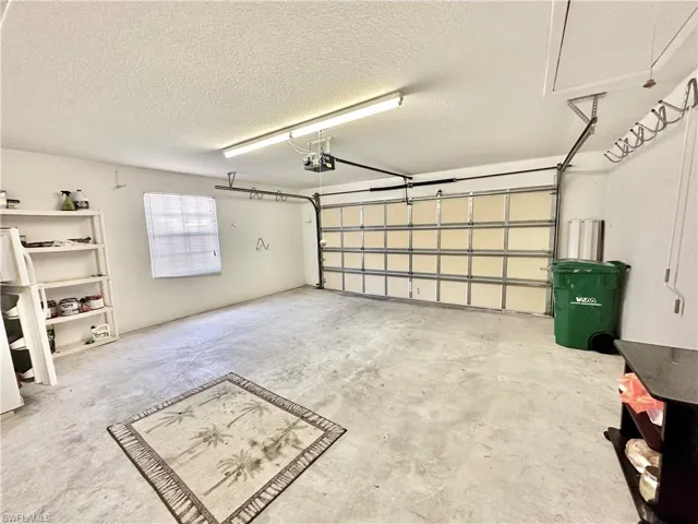 Spacious garage featuring a concrete floor, overhead lighting, an automatic garage door opener, and a window with blinds