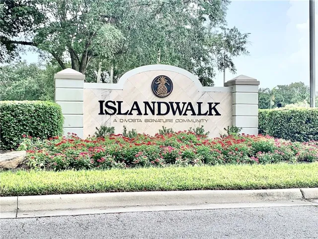 Community entrance sign featuring stacked stone columns, a carved sign with "ISLANDWALK" lettering, and an embedded pineapple emblem