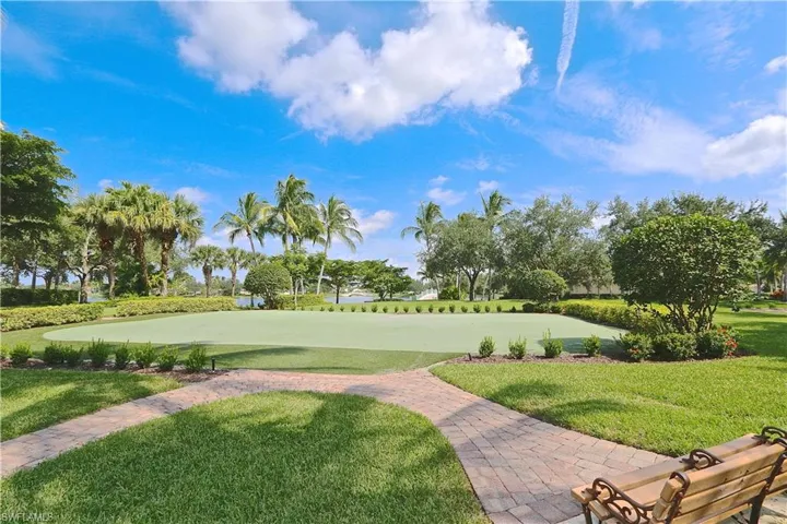 Manicured green space featuring a putting green surface, surrounded by lush landscaping and mature palm trees