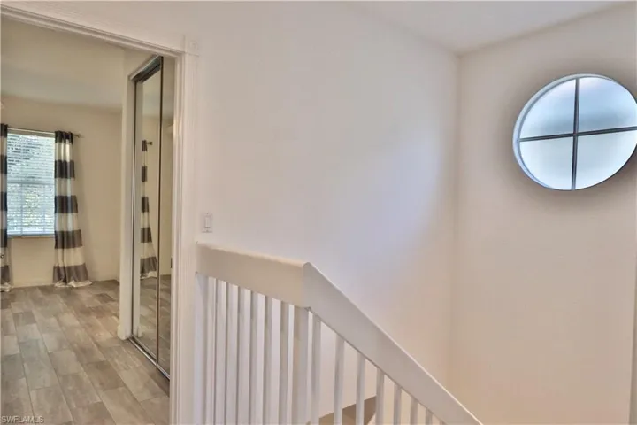Landing area featuring a distinctive circular window, white painted balusters, and a light wood-finish flooring extending into an adjacent room with a window and mirrored closet doors