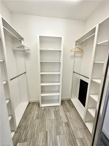 Walk-in closet featuring wood-finish flooring, white built-in shelving, hanging rods, and a central freestanding bookcase