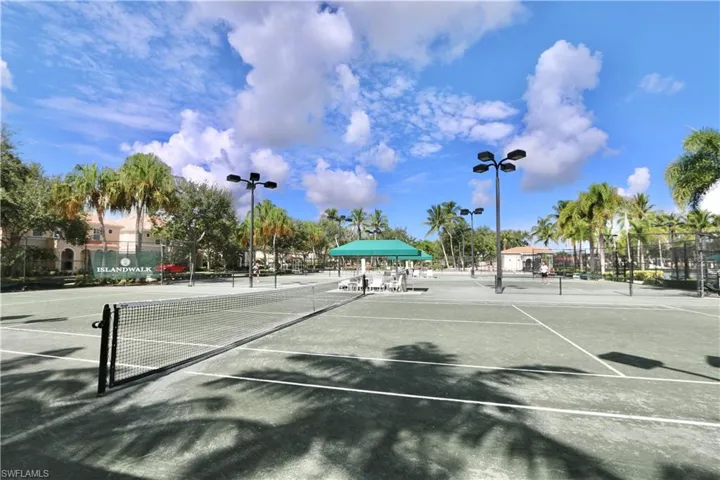 Multiple tennis courts featuring a hard court surface, perimeter fencing, and overhead lighting