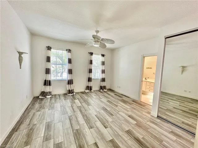 Spacious room featuring wood-finish flooring, two windows with blinds, a ceiling fan, and a mirrored closet door