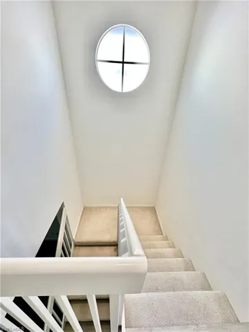 Stairwell featuring a circular transom window, white painted railings, and carpeted steps