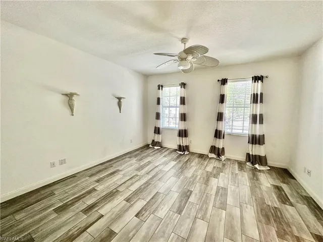 Spacious room featuring wood-finish plank flooring, two windows with blinds, a ceiling fan, and white baseboards
