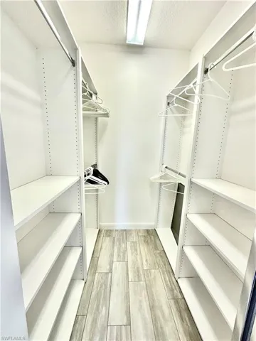 Walk-in closet featuring floor-to-ceiling white shelving, multiple hanging rods, recessed lighting, and wood-finish flooring