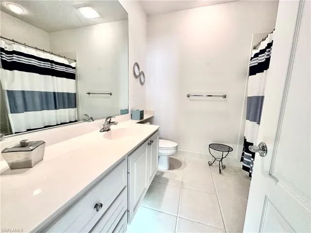Bathroom featuring a vanity with dual sinks, white cabinetry, a large wall-mounted mirror, and tile flooring