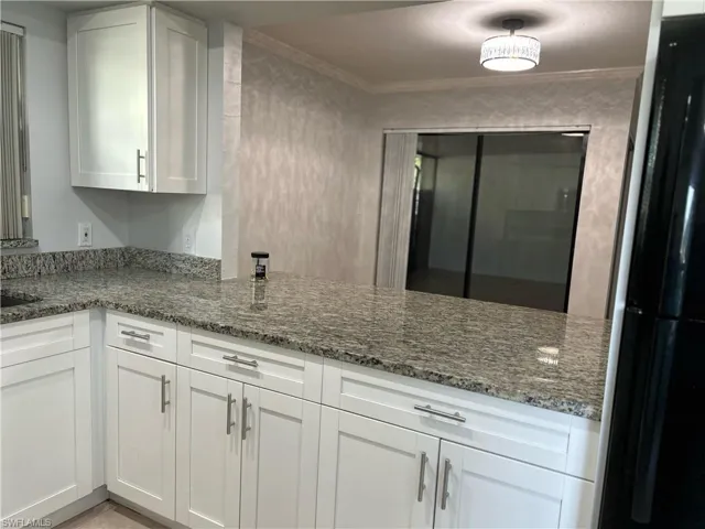Kitchen featuring white cabinetry, ornamental molding, dark stone countertops, and black refrigerator