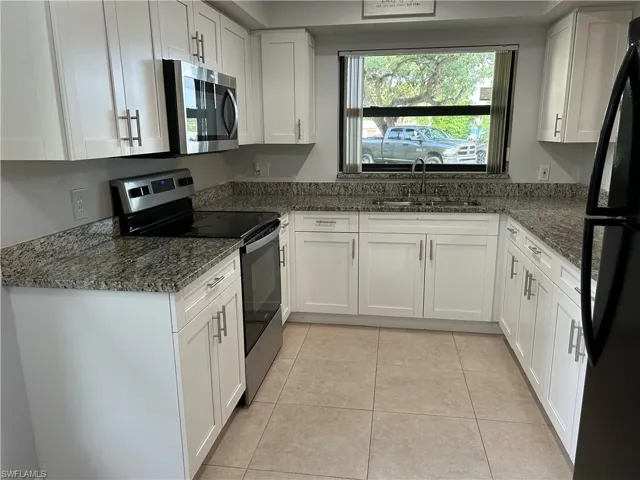 Kitchen featuring light tile flooring, dark stone countertops, sink, white cabinets, and appliances with stainless steel finishes