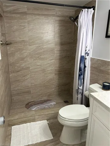 Bathroom with tile walls, vanity, curtained shower, and toilet