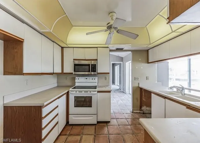 Kitchen with white cabinets, ceiling fan, tile flooring, sink, and electric stove
