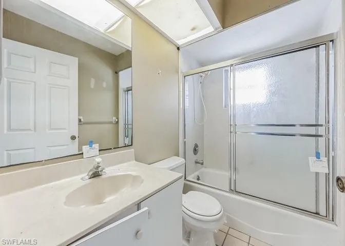 Full bathroom featuring tile flooring, combined bath / shower with glass door, vanity, and toilet